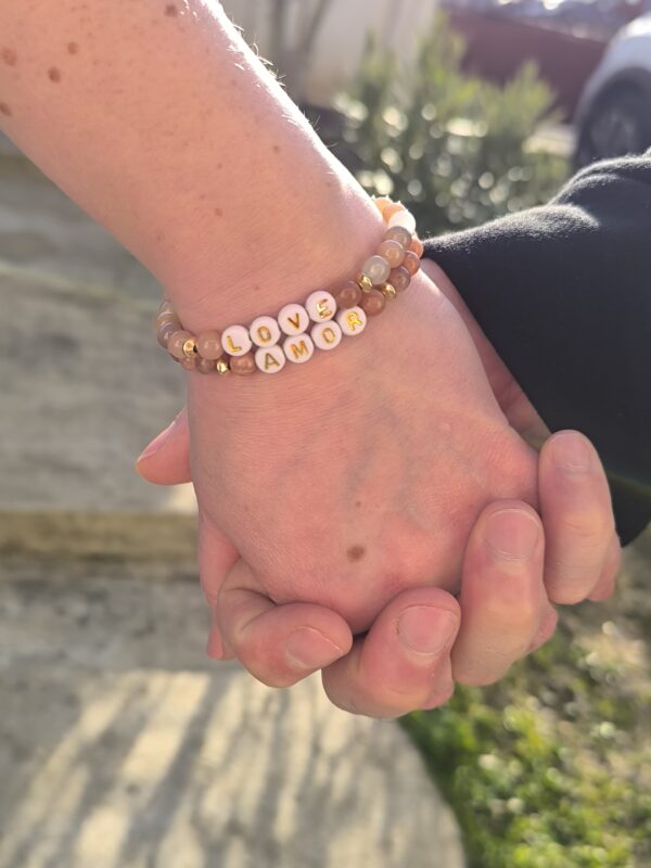 Deux mains se tenant, avec Bracelet en pierre du soleil avec inscription Love et bracelet, en pierre de lune avec inscription AMOR. Réalisé par Main de Crystal