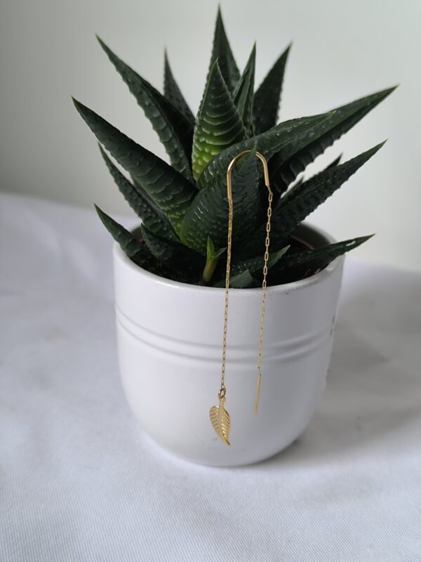 Boucle d'oreille chaine avec une breloque feuille, en acier inoxydable, créée par Main de Crystal, sur un cactus.