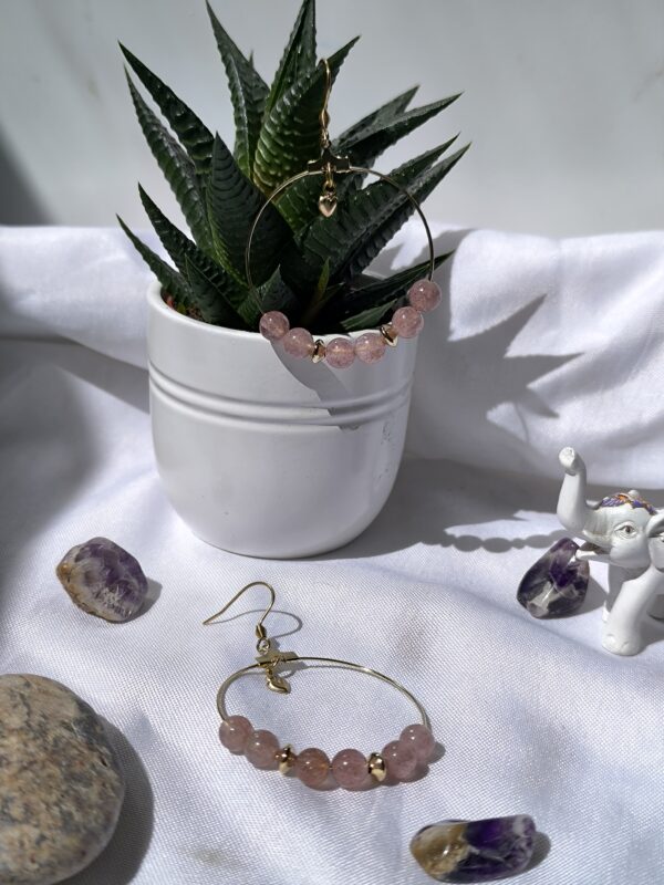 Boucles d'oreilles créoles en acier inox et quartz fraise et breloque cœur, créé par Main de Crystal, à coté d'une fleur succulante