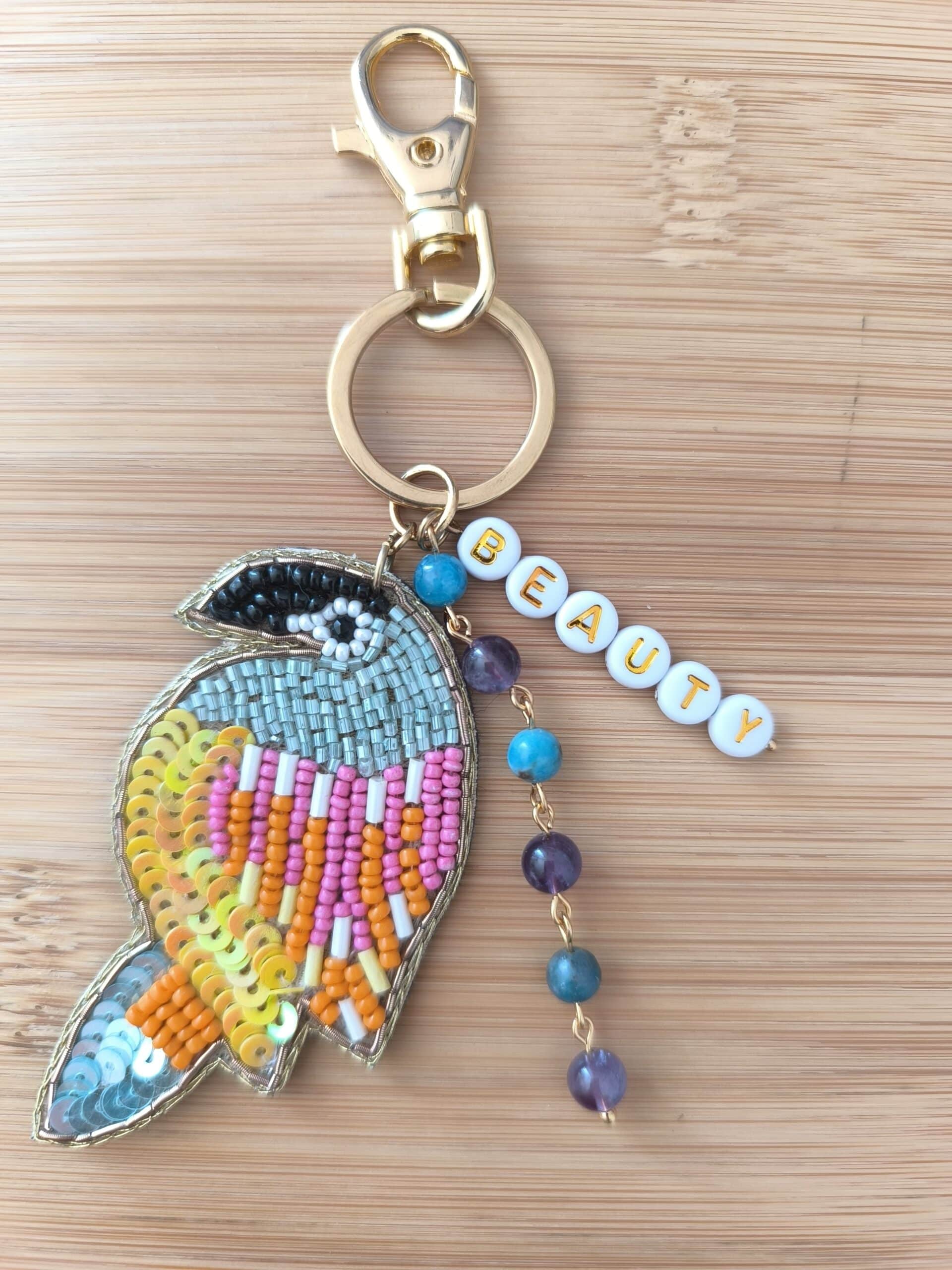 Bijou de sac en laiton doré, avec un perroquet en perles tressées, des lettres en perles faisant le mot "Beauty" et 4 pierres en améthyste et apatite