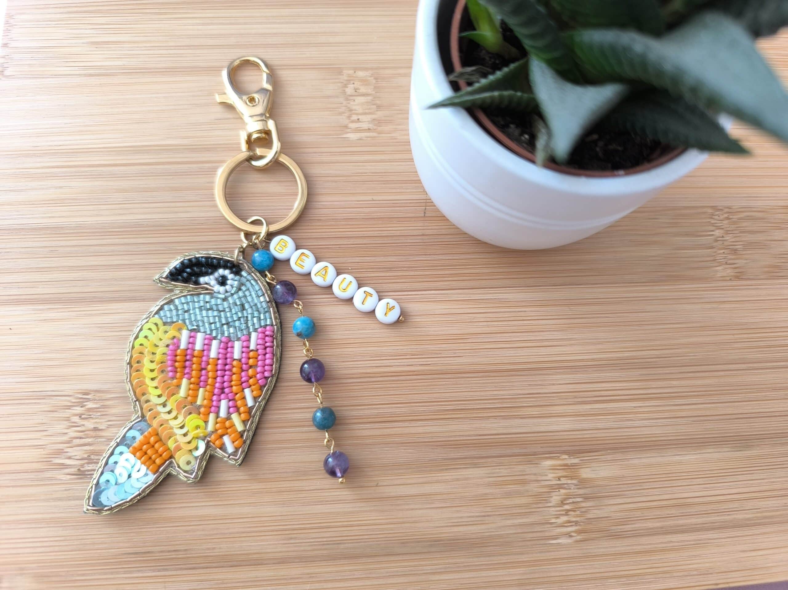 Bijou de sac en laiton doré, avec un perroquet en perles tressées, des lettres en perles faisant le mot "Beauty" et 4 pierres en améthyste et apatite - Réalisé par Main de Crystal